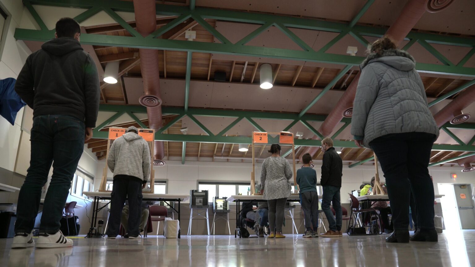 Voters stand in lines behind tables inside a large room.