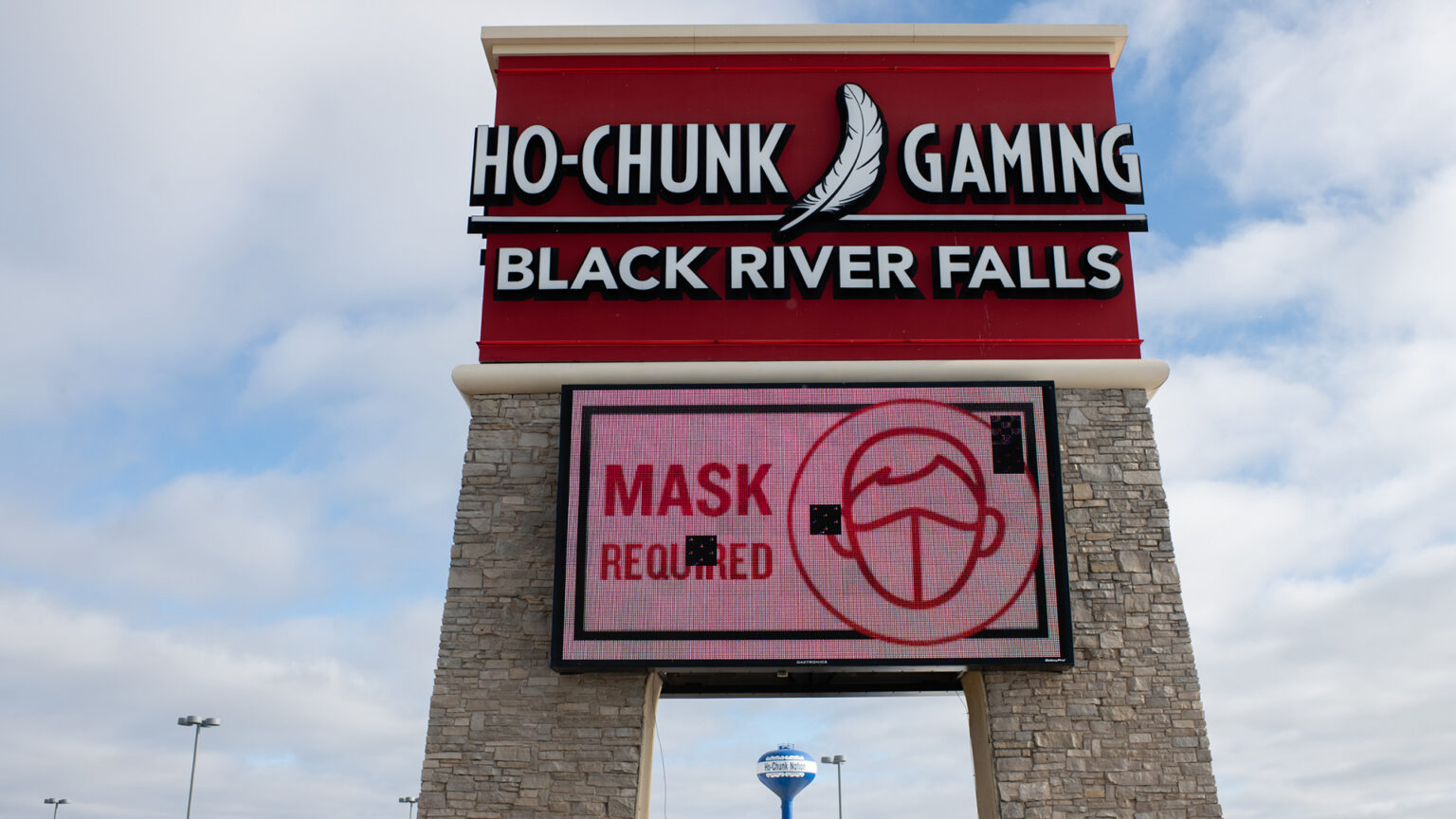 A large exterior sign for Ho-Chunk Gaming Black River Falls is situated above an electronic screen with an illustration of a face covered with a mask and the words Mask Required.