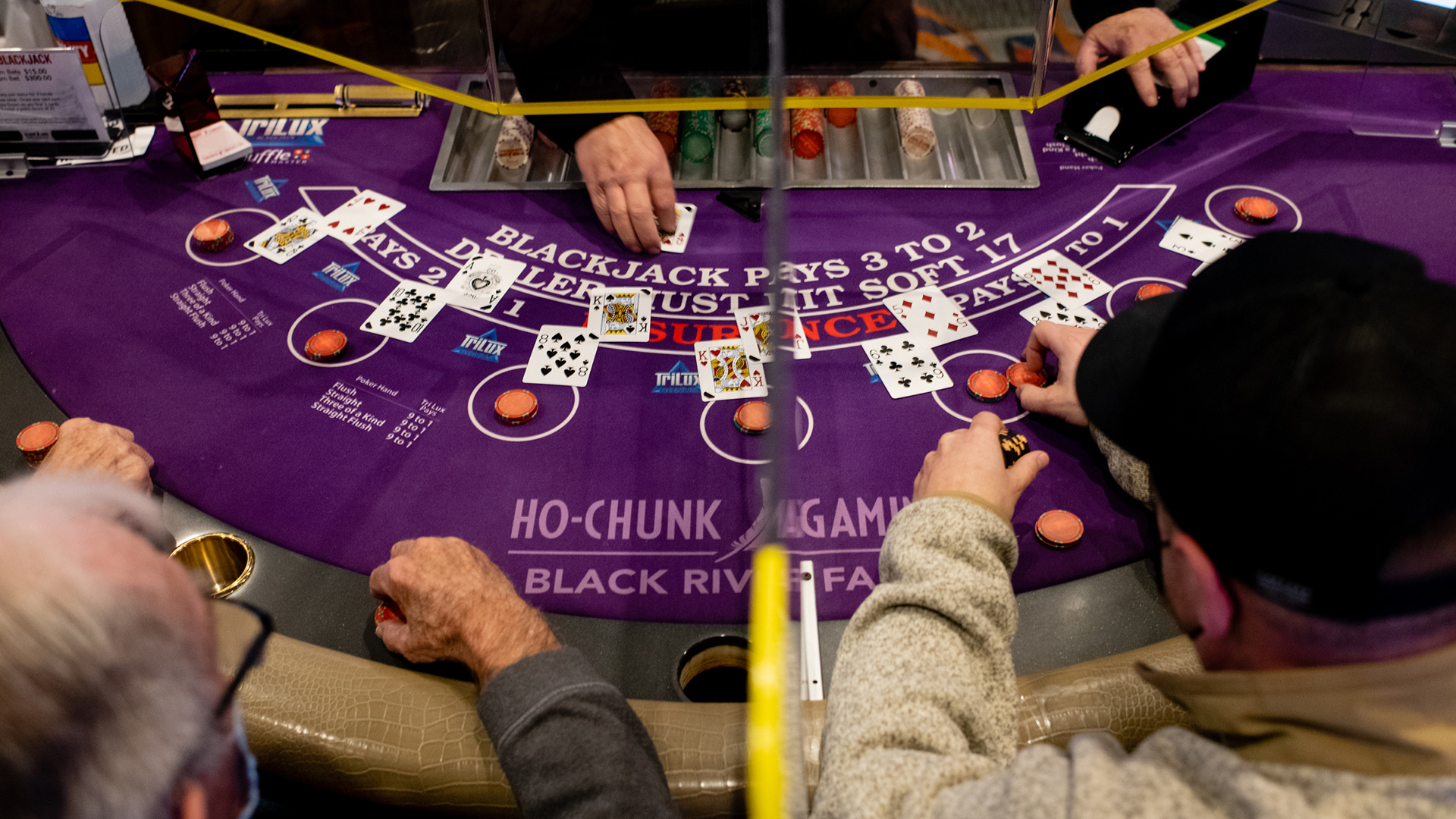 An overhead photo shows two people leaning over a blackjack table with cards and chips.