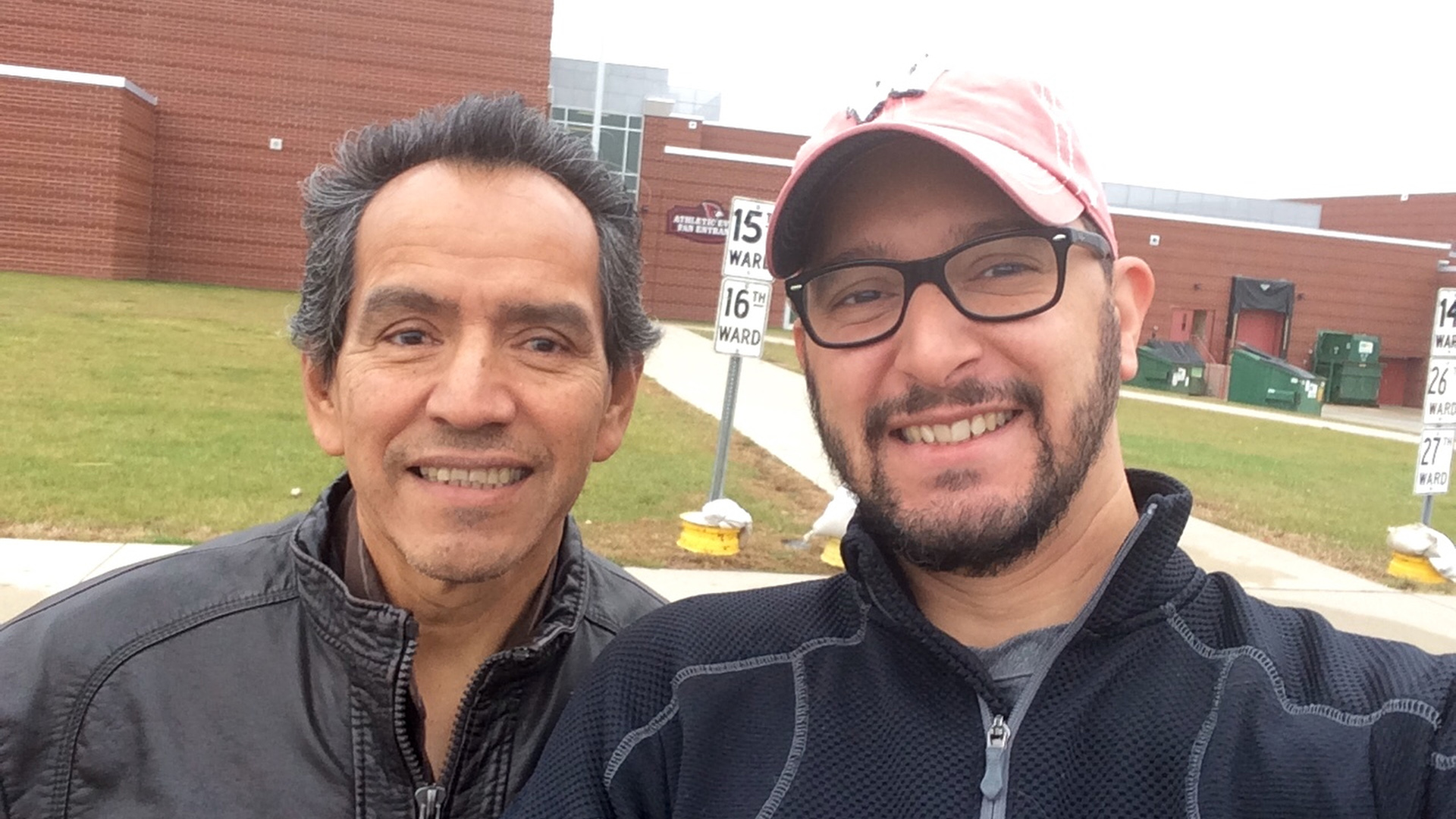 Carlos Muñoz Sr. and Carlos Muñoz Jr. stand in front of a school building.