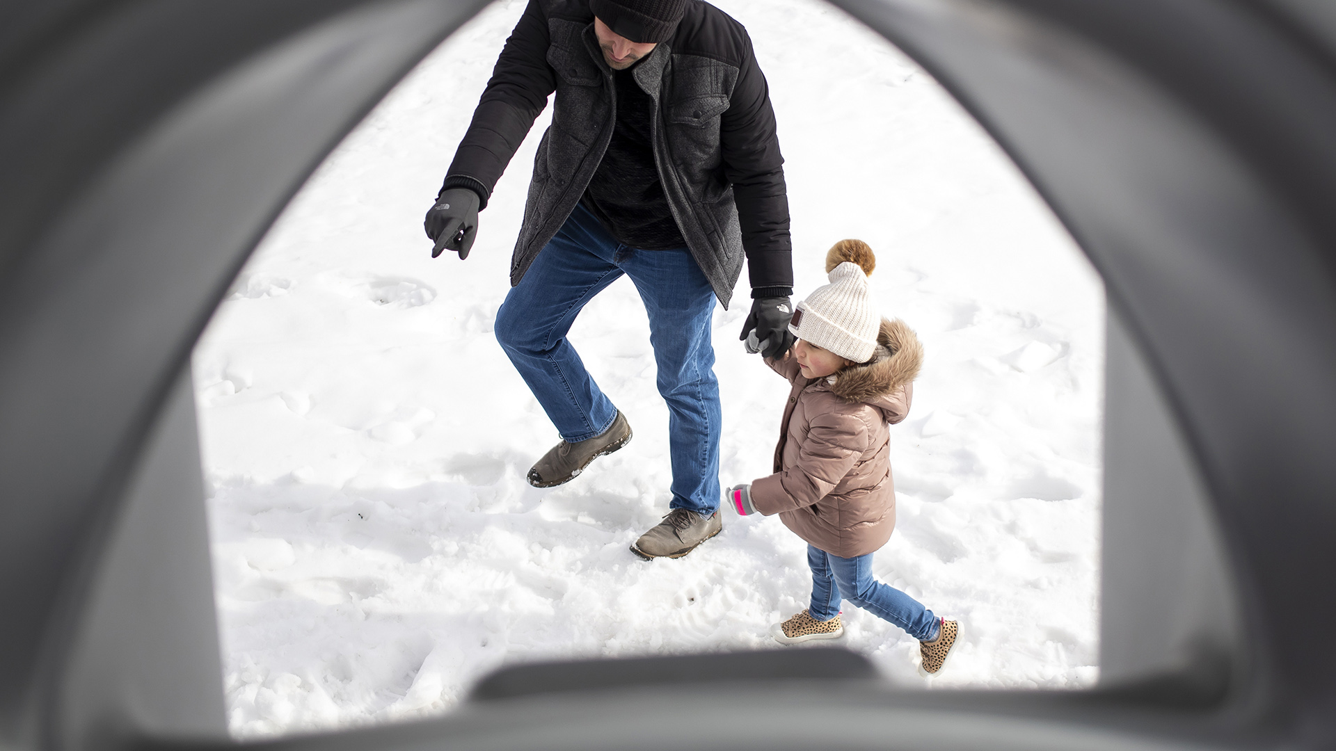 Mario Gonzalez holds the hand of his daughter as the walk across snowy ground as seen through playground equipment.
