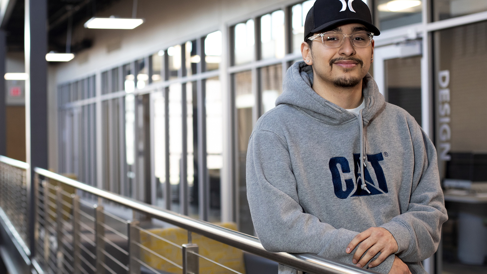 Emmanuel Vargas stands next to a railing for an indoor walkway balcony, with glass walls and doors in the background.