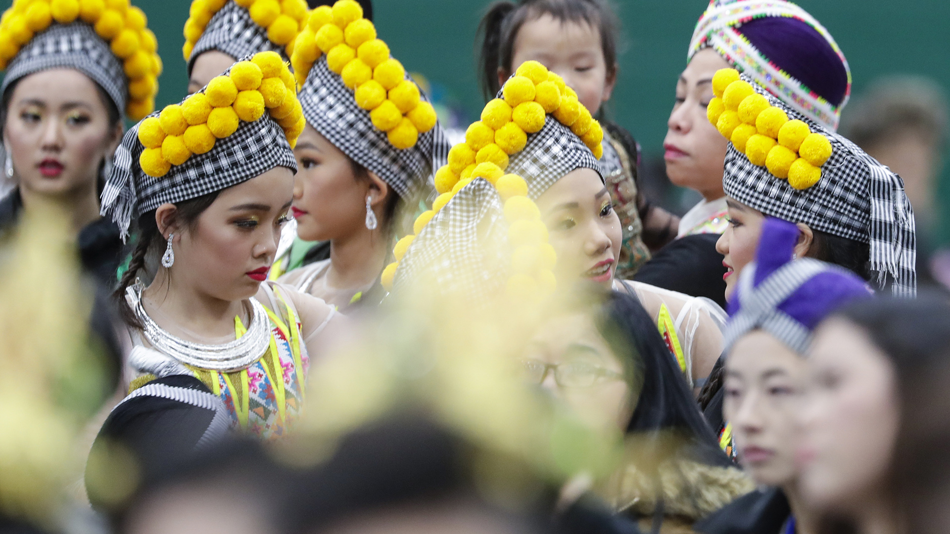 Performers wearing traditional headwear and other costume elements are crowded together in a room.