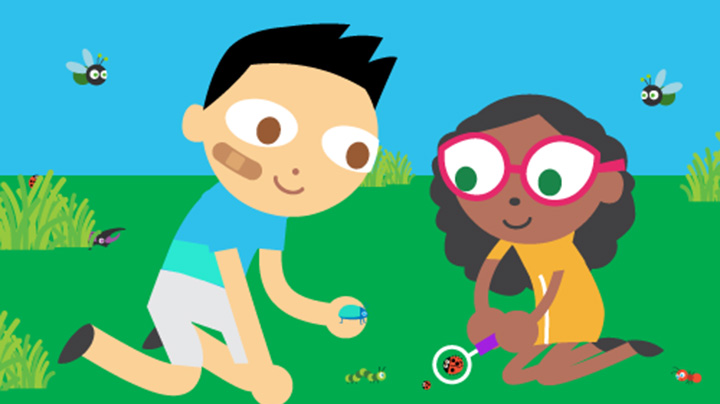 Two children sit in the grass examining bugs with a magnifying glass
