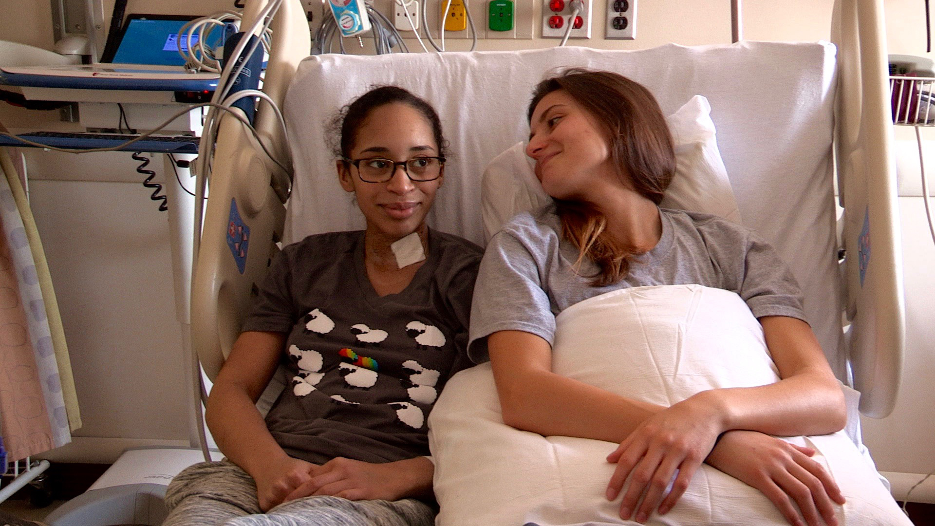 Two women sit next to each other in a hospital bed.