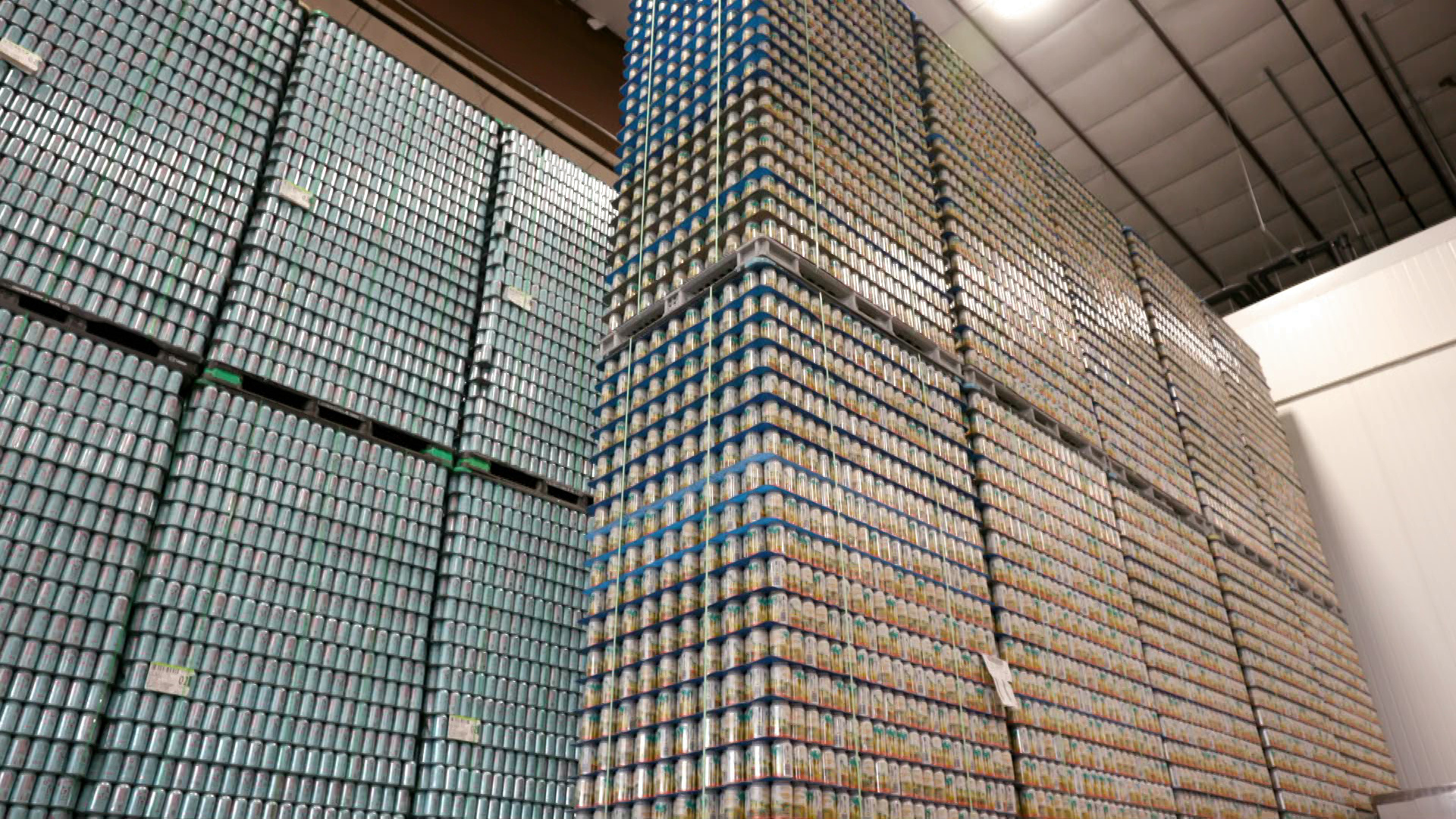 Pallets of cans sit stacked from floor to ceiling in a warehouse-sized room.
