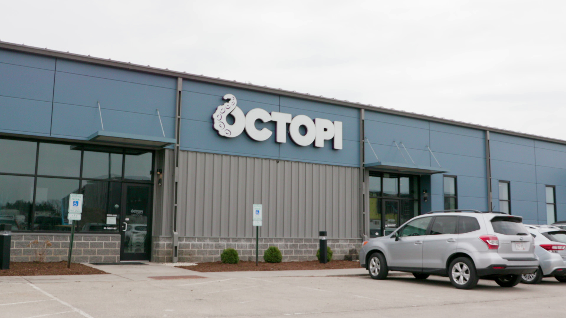A sign that reads "Octopi" is at the front of a single-story building with blue siding around multiple windows, with cars parked in front.