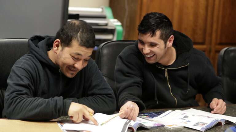 Hedaiatullah Azim and Mohammad Ali Afshar sit at a table and, while smiling, point at a book they're studying.