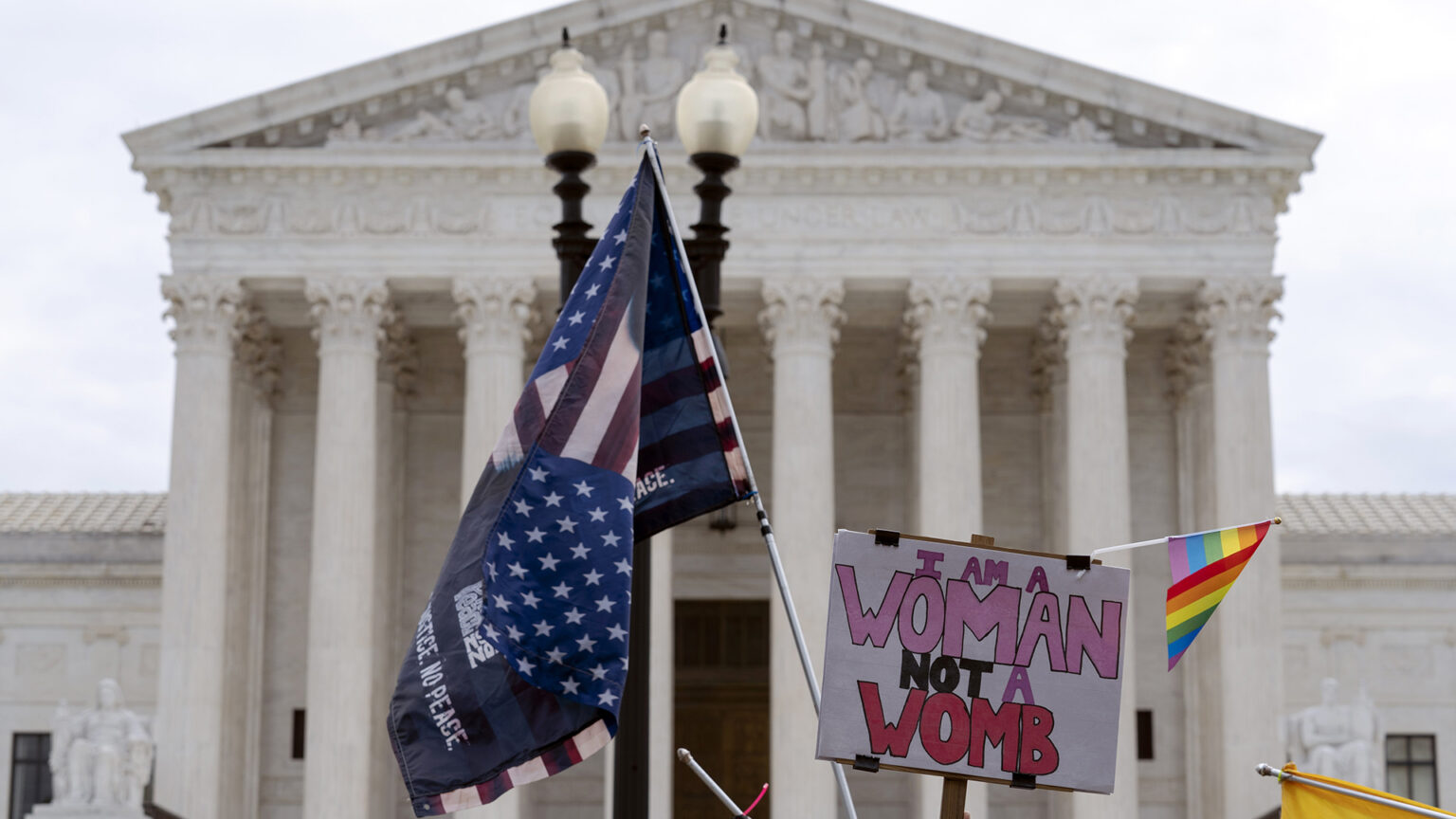 Signs and flags are held in the air in front of the U.S. Supreme Court building.