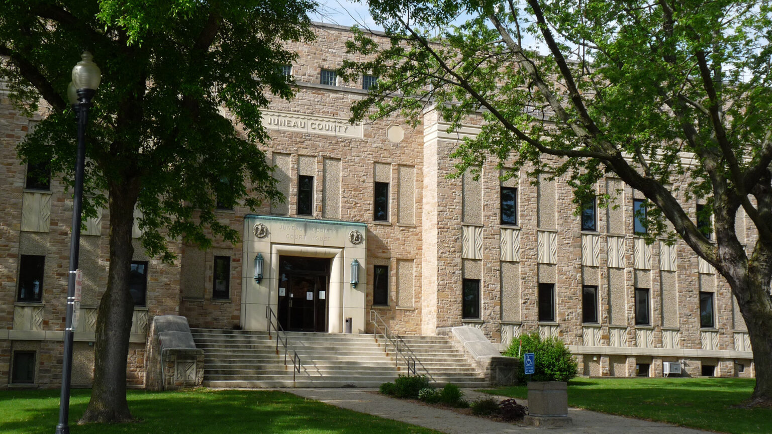 Trees stand in front of a three-story stone masonry building with art deco design elements.