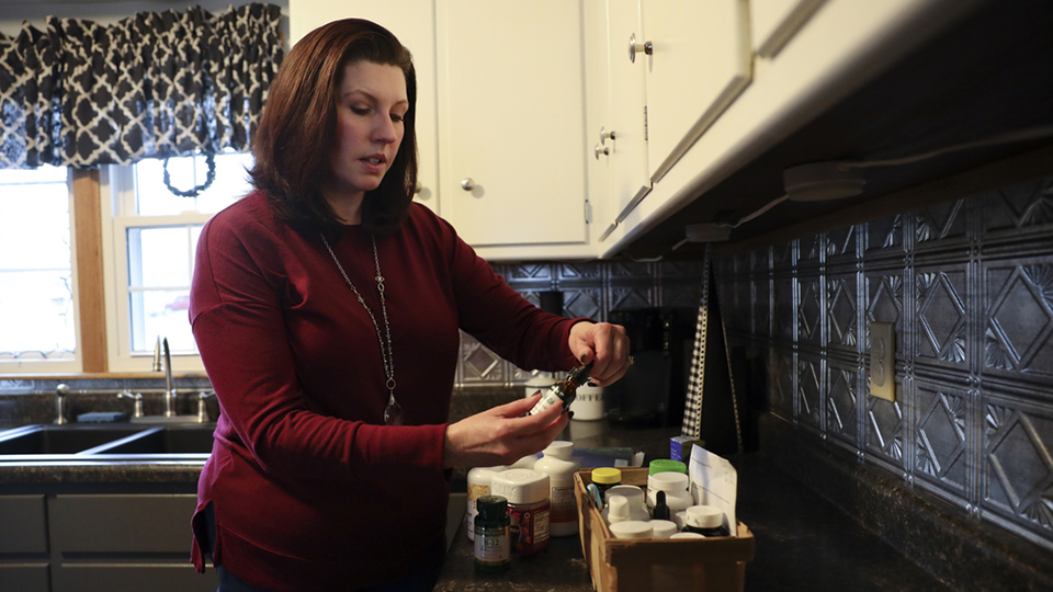 Shelbie Bertolasi stands at a kitchen countertop and holds a vial above a cluster of bottles and other containers.