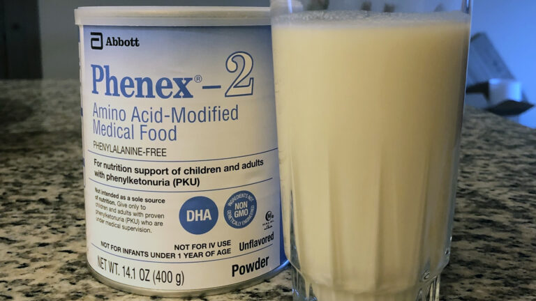 A can of formula powder for patients with phenylketonuria and a glass of the formula sit on a counter