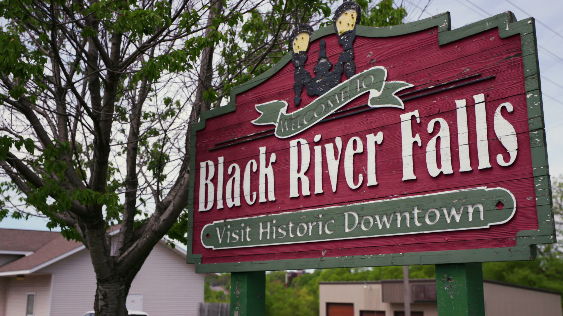 A weathered wooden sign reads "Welcome to Black River Falls ⁠— Visit Historic Downtown."