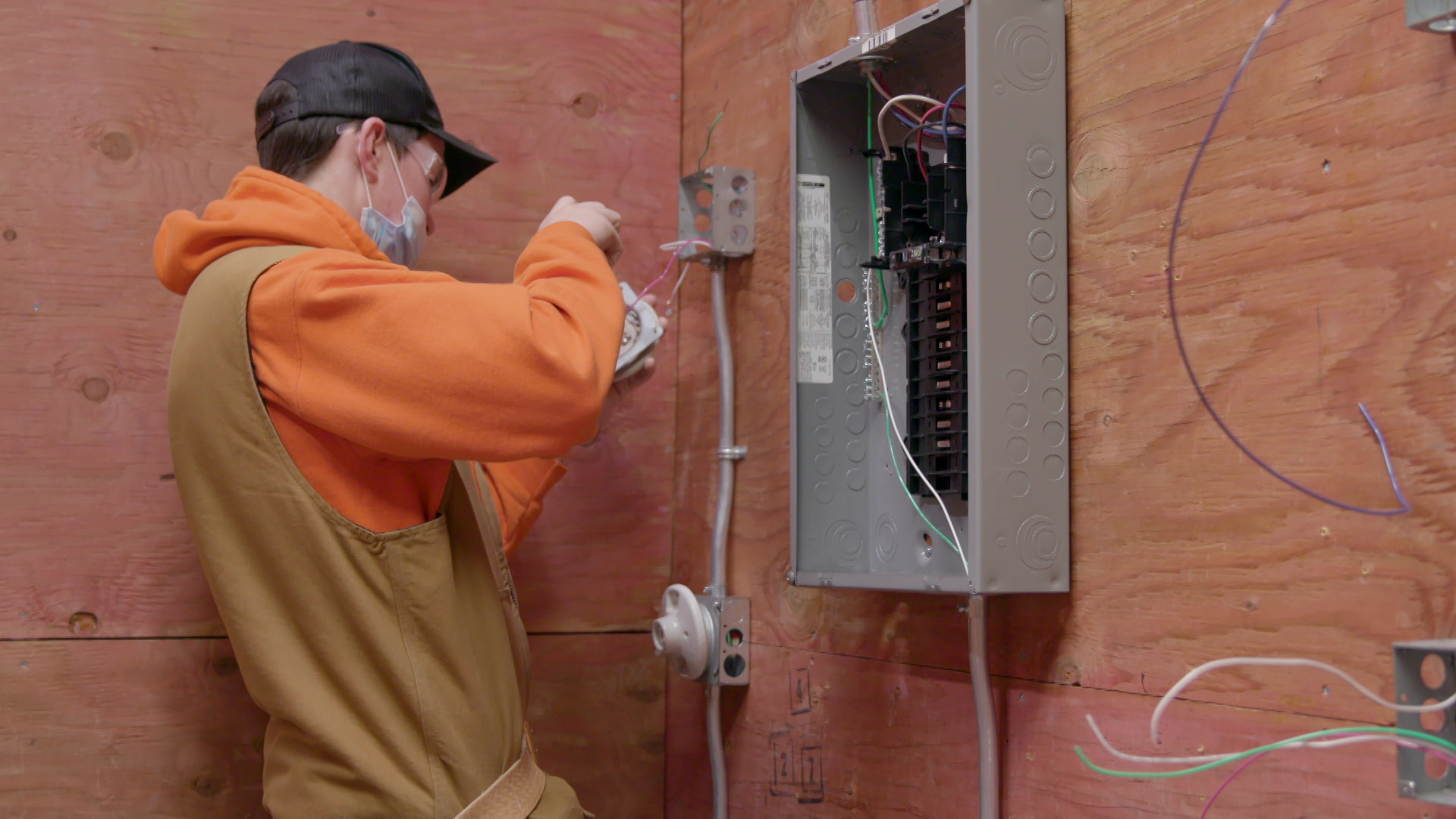 Jack Harkner trains to be an electrician in a room with plywood walls and an electrical box at Fox Valley Technical College in Appleton.
