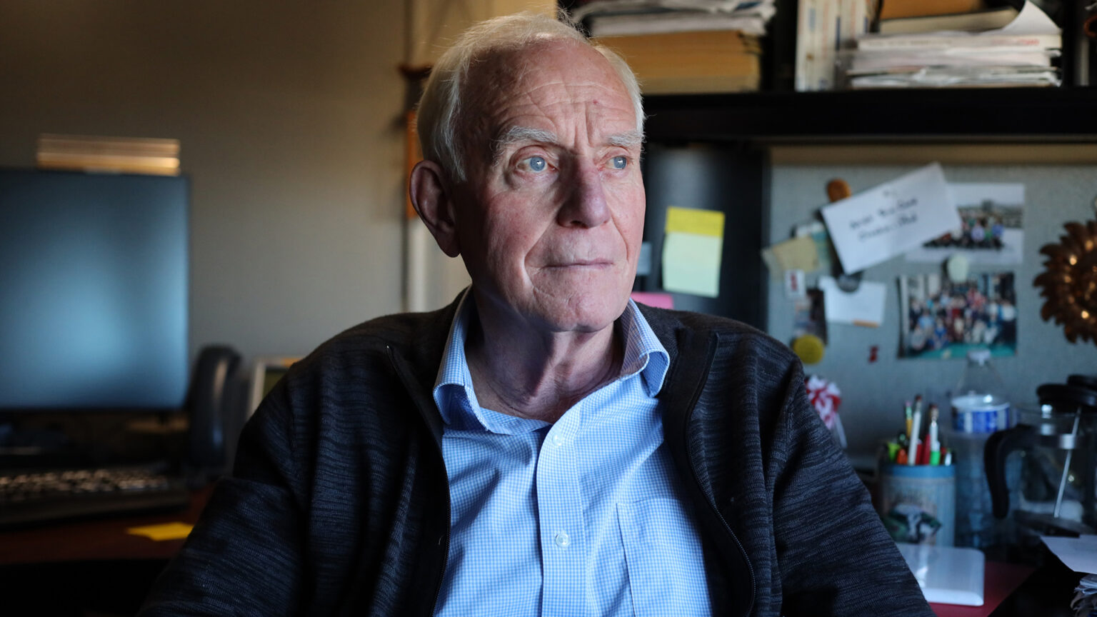 Doug Laube sits in an office with a computer, stacks of paper and other items in the background.