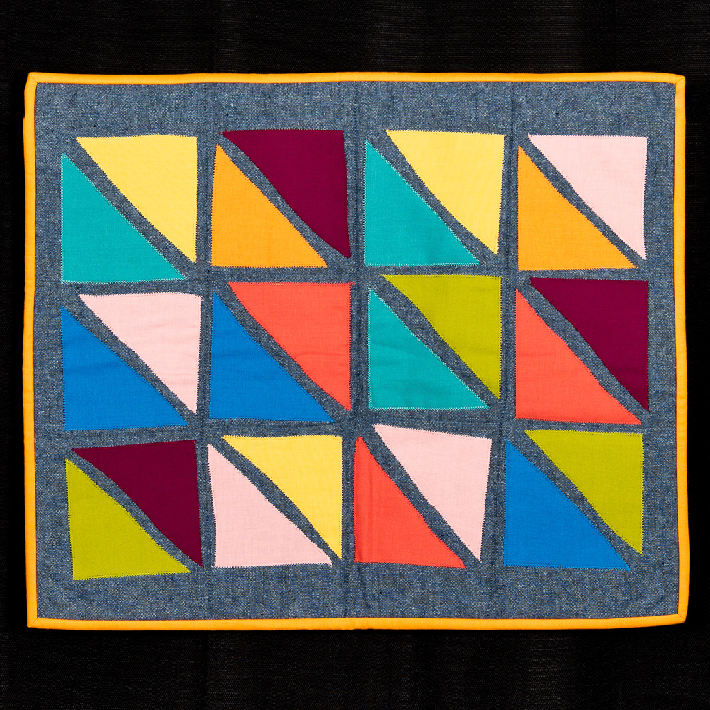 A quilt decorated with a colorful grid of squares made up of half triangles
