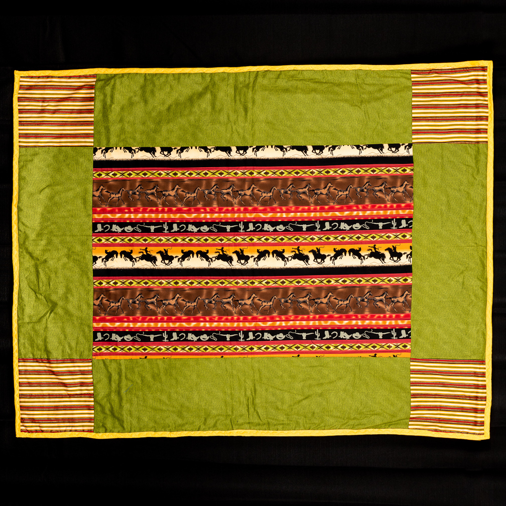 A green quilt with patterned squares in the corners and center.