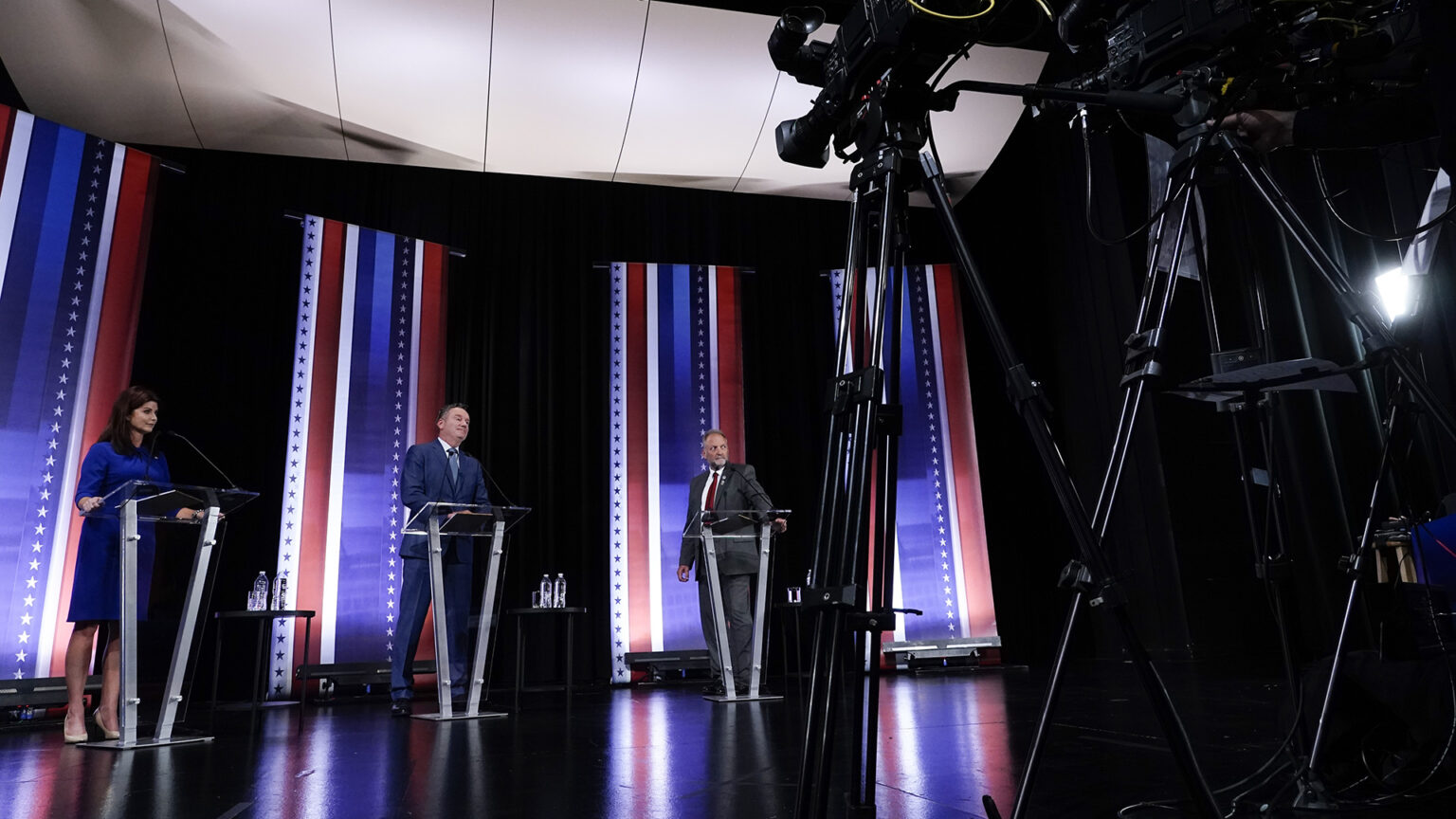 Rebecca Kleefisch, Tim Michels and Timothy Ramthun stand behind podiums on a stage facing television cameras.