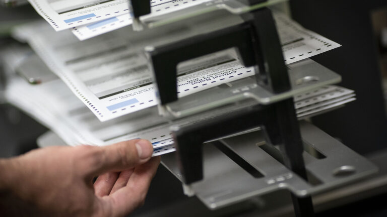 A hand holds a group of ballots stacked in a shelving system.
