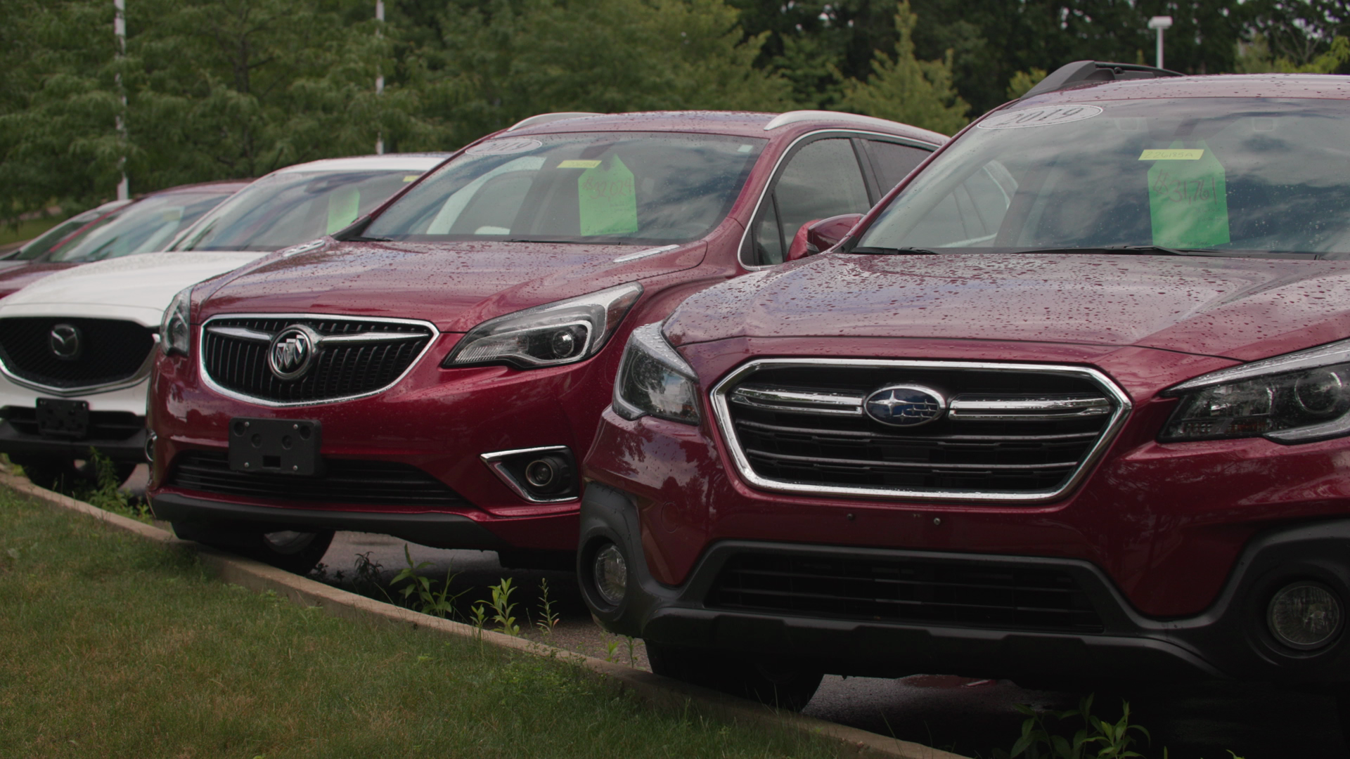 A row of parked SUVs for sale show price takes behind their front windshields.