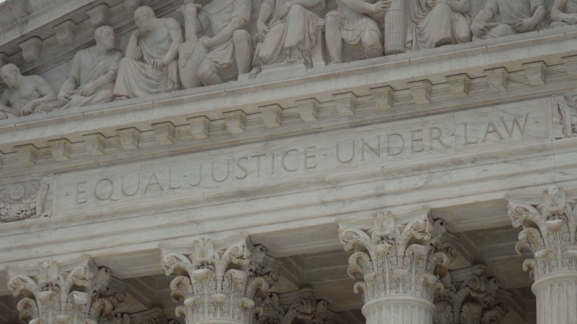 A carved marble façade atop a row of columns reads "Equal Justice Under Law" with Classical-style statues arrayed above.
