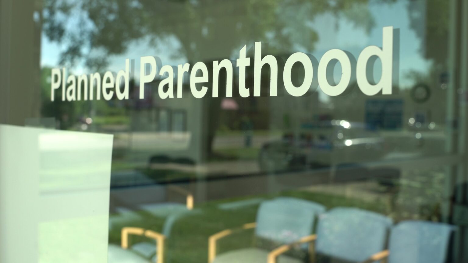 A stencil sign on a window reads Planned Parenthood with empty chairs in a waiting room visible through the glass.