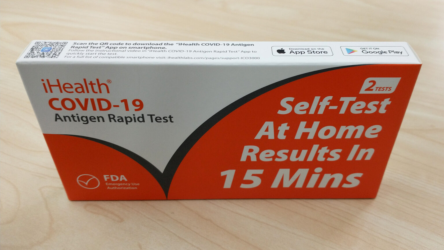 An iHealth COVID-19 Antigen Rapid Test box with packaging that reads Self-Test At Home Results in 15 Mins sits on a table.