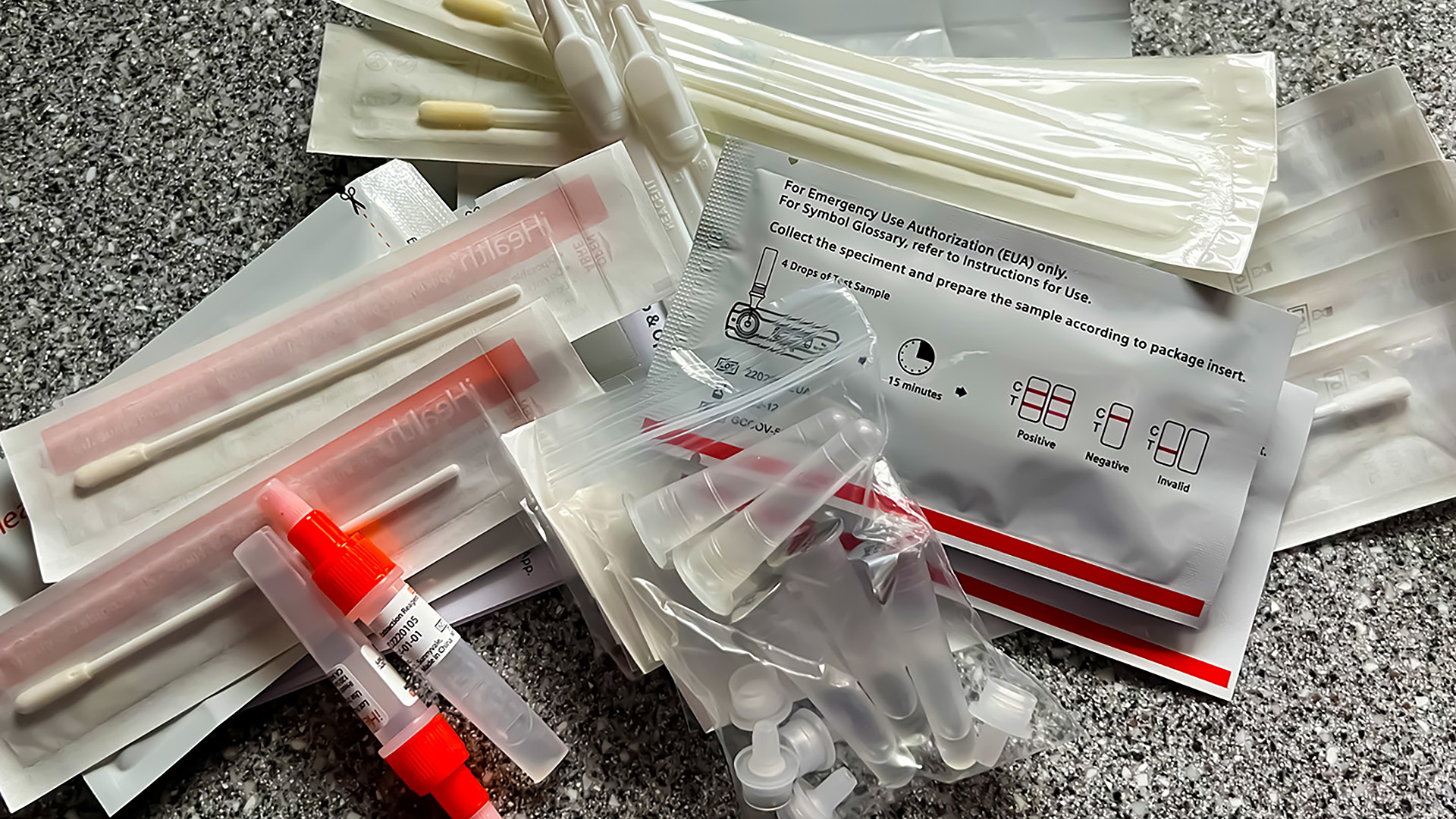 Swabs, vials and other elements of at-home COVID-19 antigen test kits sit on a counter.