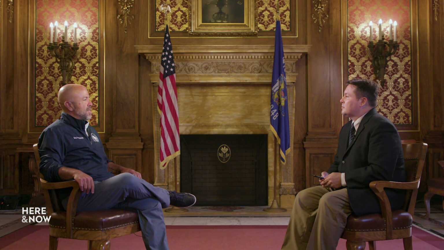 Jim Steineke and Zac Schultz sit in chairs in a room in the Wisconsin State Capitol with a wood-paneled fireplace, sconces and the U.S. and state flags in the background.