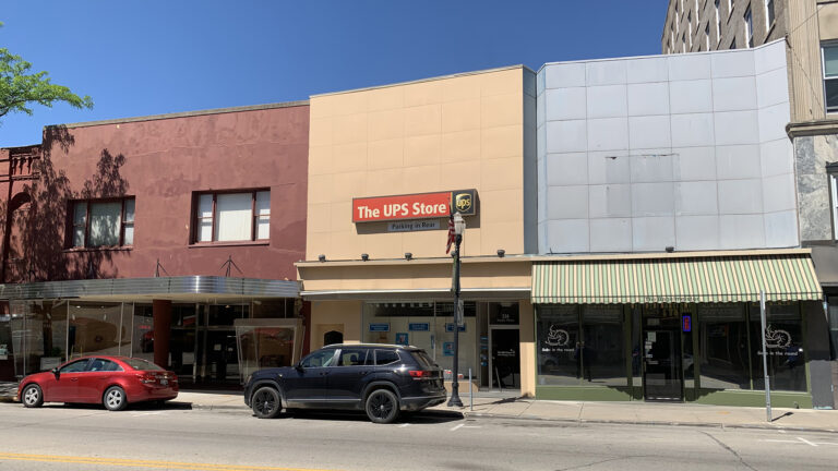 Cars are parked on the side of the street next to a series of storefronts, including one with a sign reading The UPS Store.