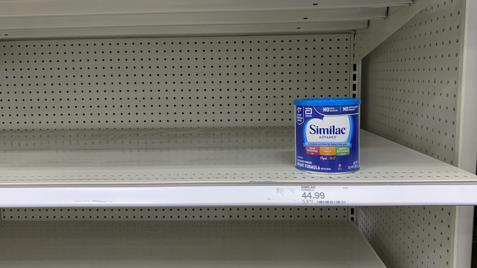 A single canister of formula sits on an otherwise empty store shelf.