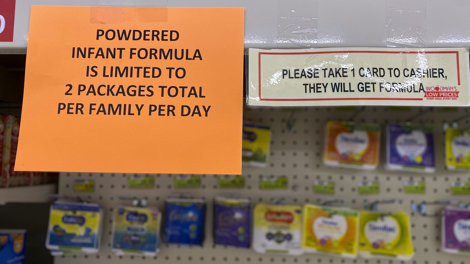 Printed signs on a grocery store shelf read "Powdered infant formula is limited to 2 packages total per family per day" and "Please take 1 card to cashier, they will get forumla."