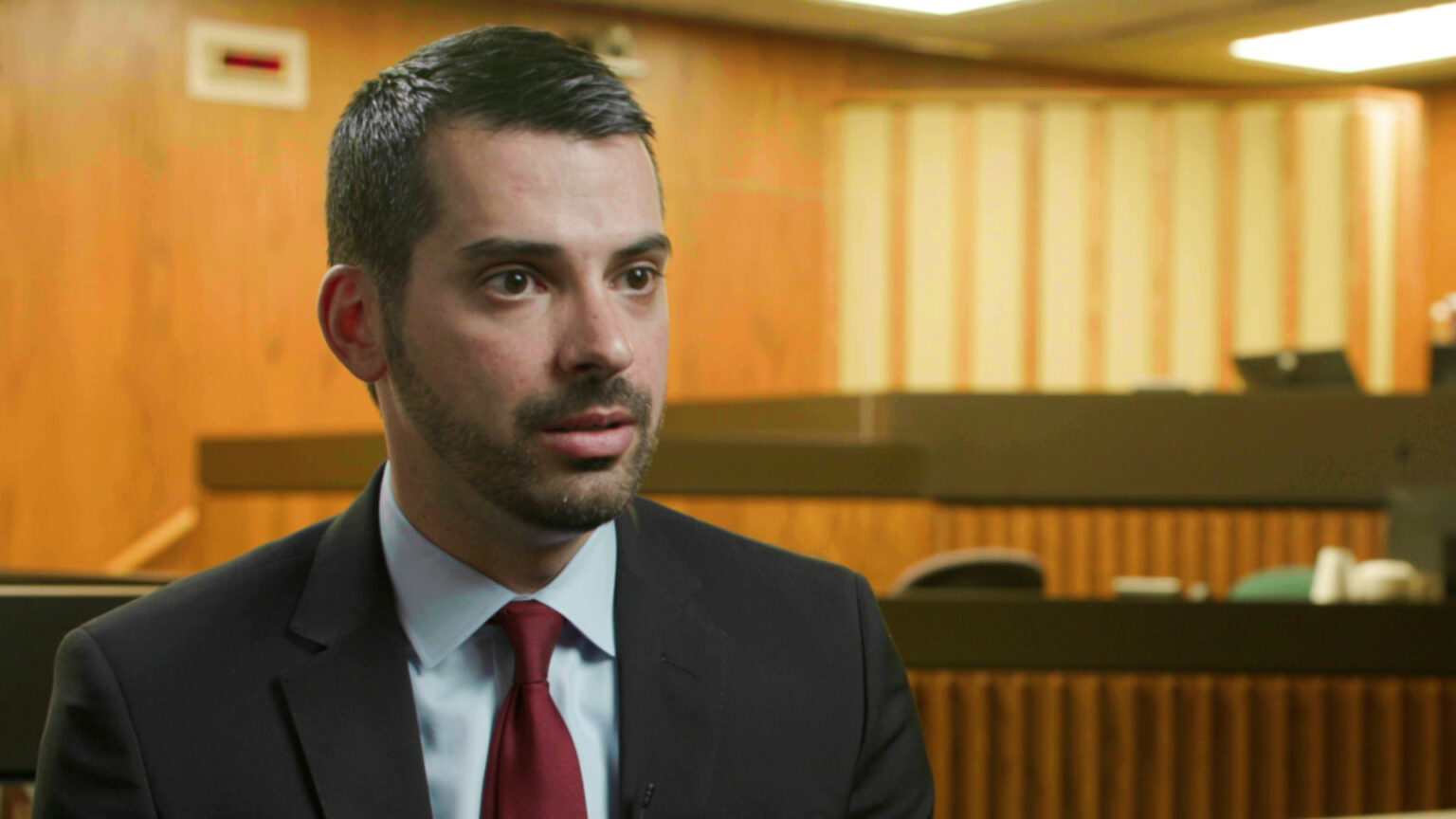 Eric Toney sits in a courtroom with tables and a raised judge's bench in the background.