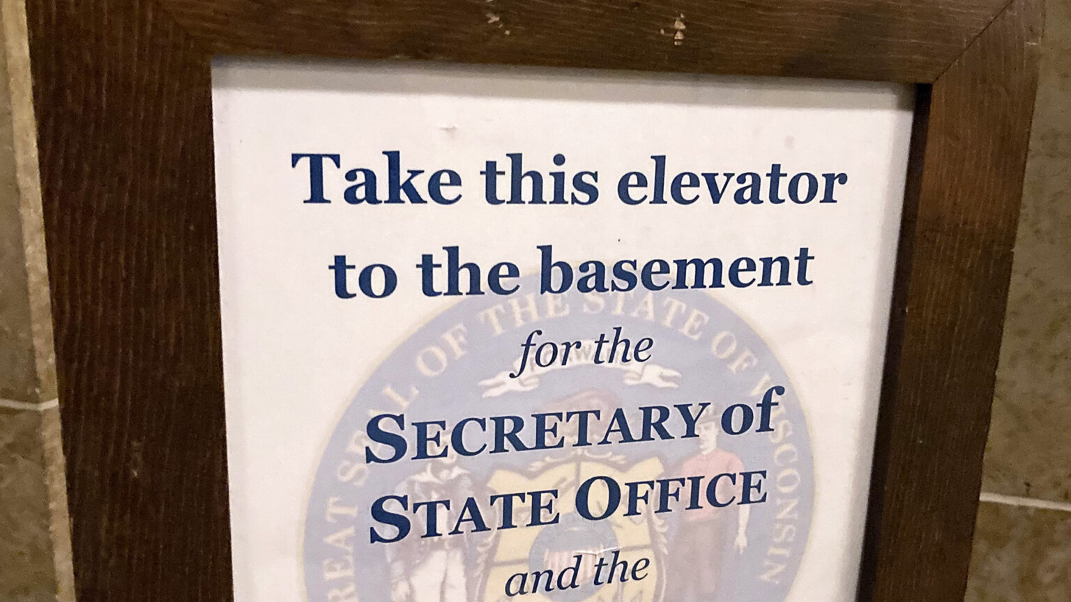 A sign in the Wisconsin State Capitol reads Take this elevator to the basement for the Secretary of State Office and the... with the remaining portion out of frame.