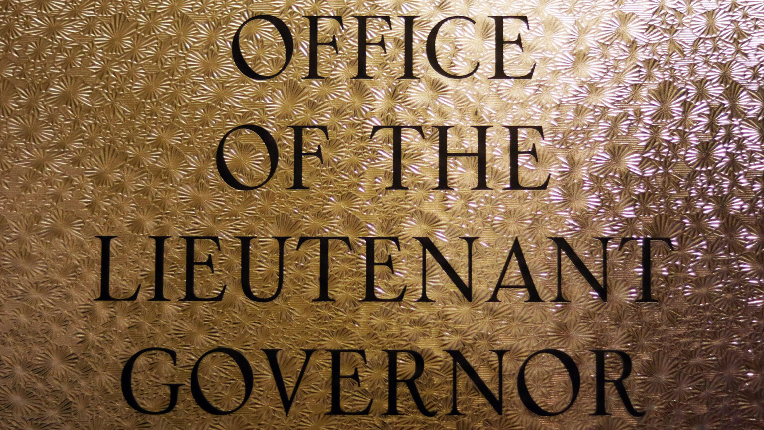 A door stencil reads Office of the Lieutenant Governor with light shining through patterned glass. 