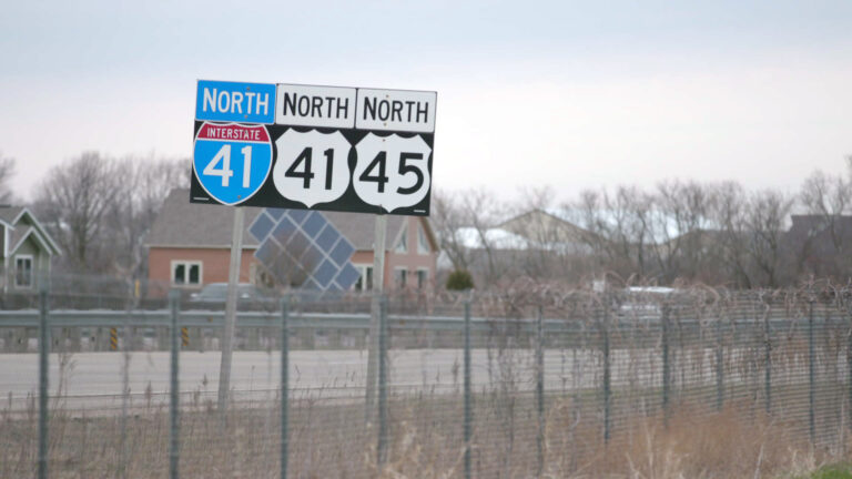 Highway signs for U.S. Interstate 41 North as well as U.S. Highway 41 North and U.S. Highway 45 North stand next to a road in spring, with houses and leafless trees in the background.