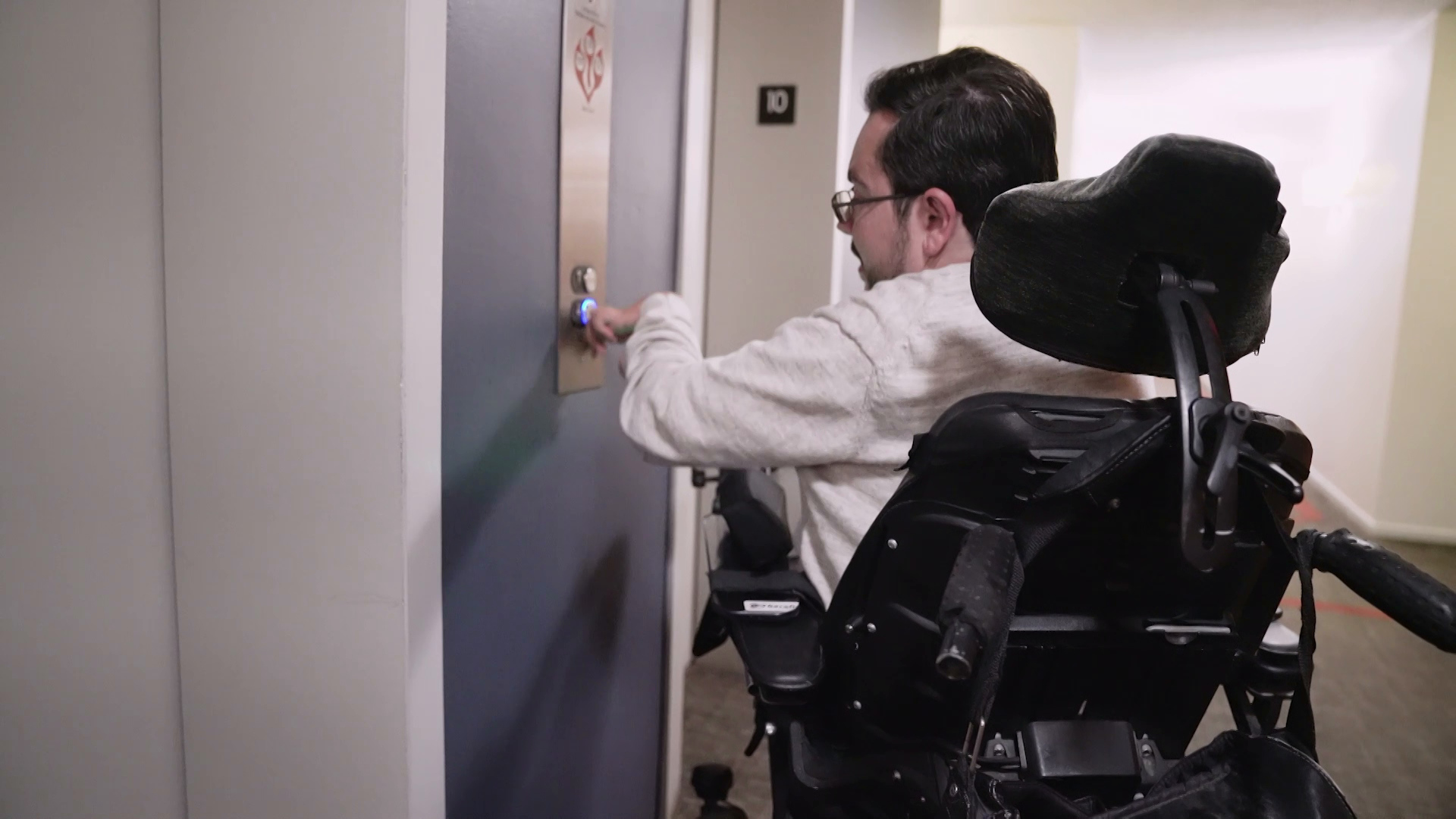 William Crowley pushes an elevator button while in his wheelchair.