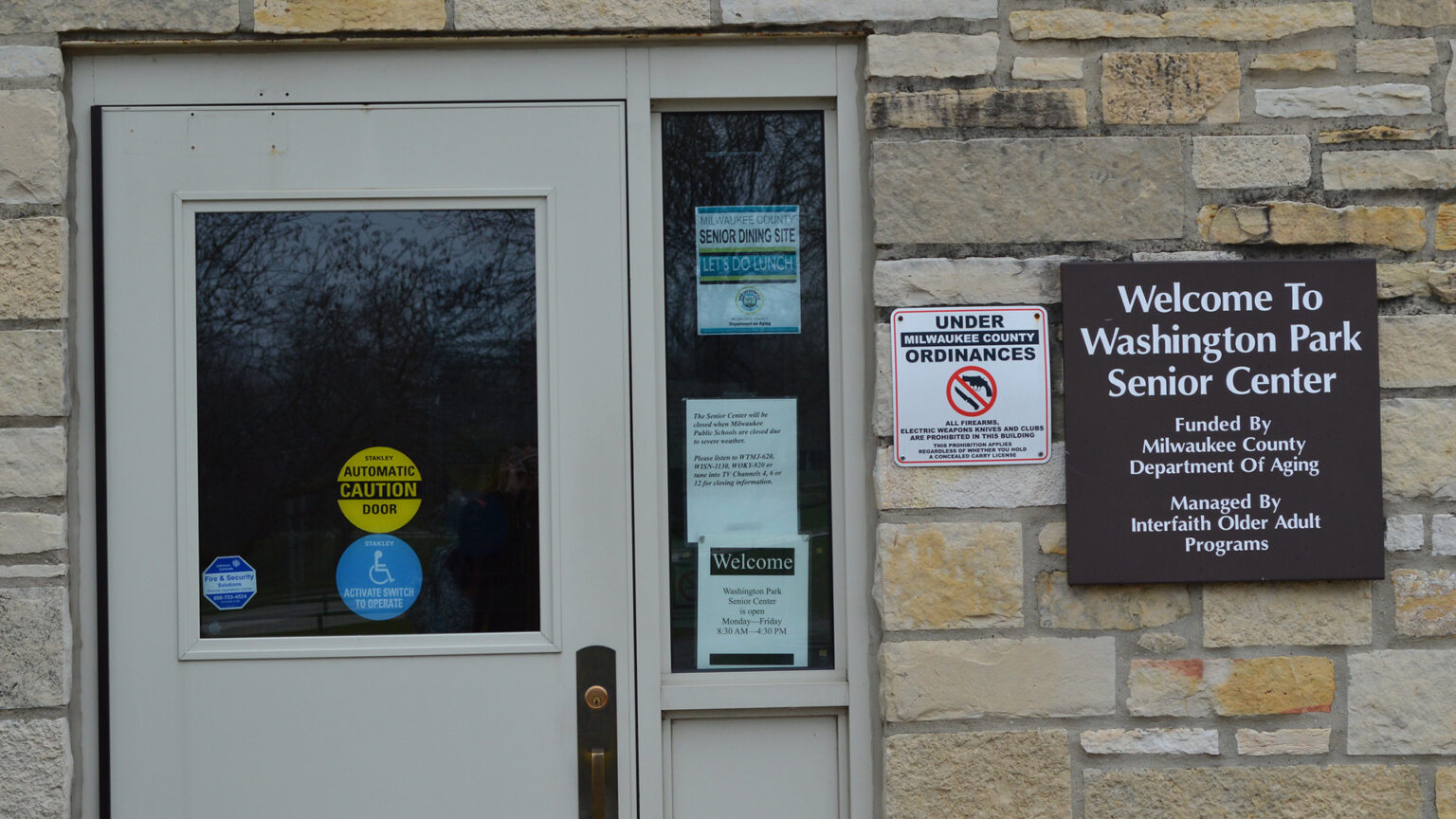 A sign mounted on a masonry wall next to a door with glass windows reads Welcome to Washington Park Senior Center.