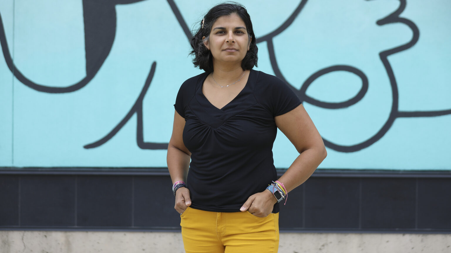 Shefaali Sharma stands in front of an abstract mural on the side of a building.