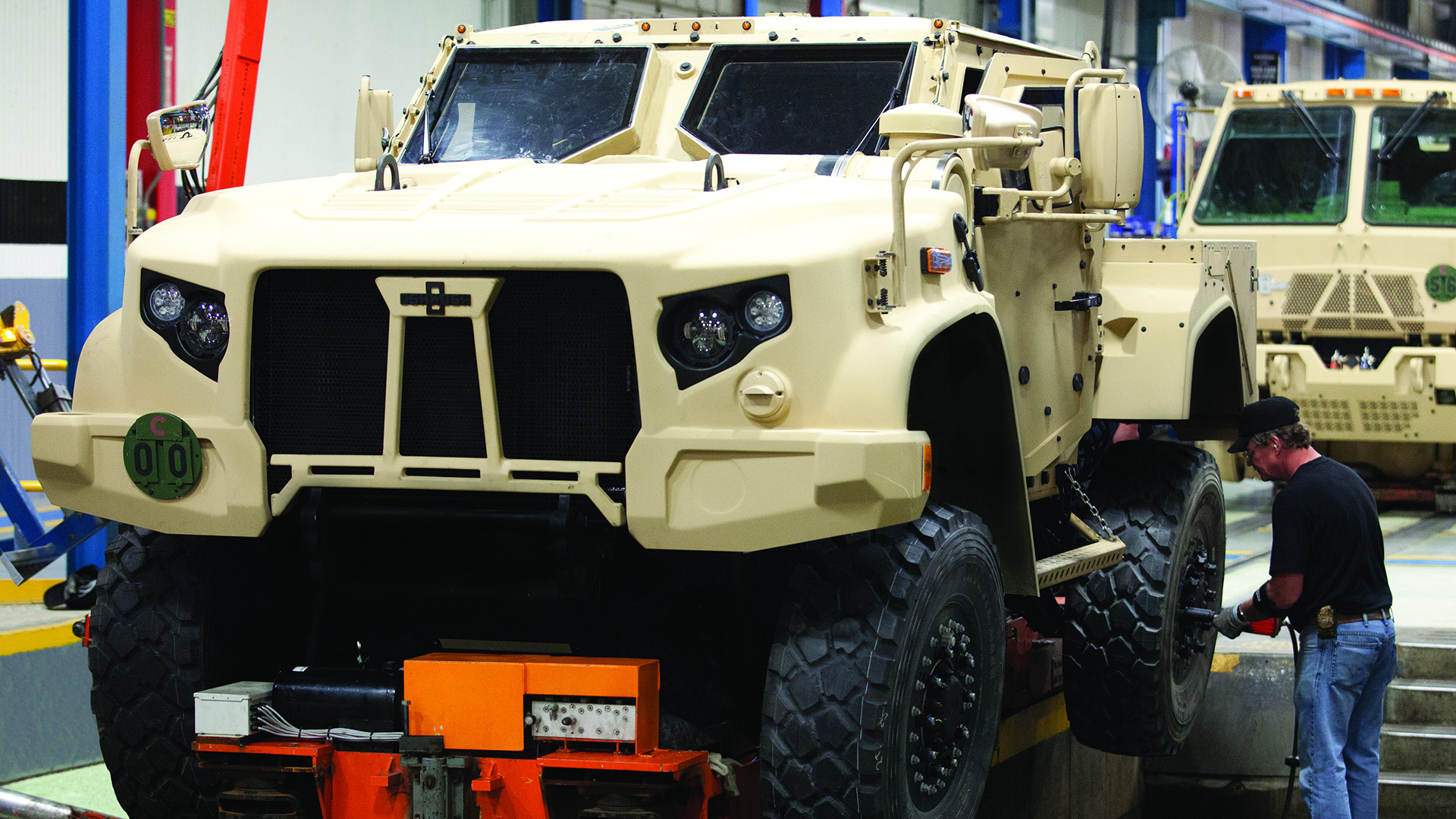 An auto manufacturing plant employee works on the wheel of a Joint Light Tactical Vehicle on a factory assembly line.
