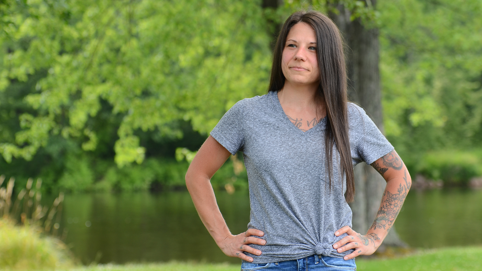 Britnie Remer poses for a portrait with a tree and riverbank in the background, with more foliage on its opposite shore.