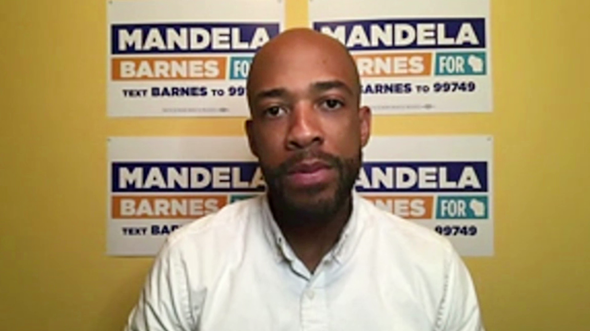 Mandela Barnes speaks while looking at a camera during an online interview with campaign posters in the background.
