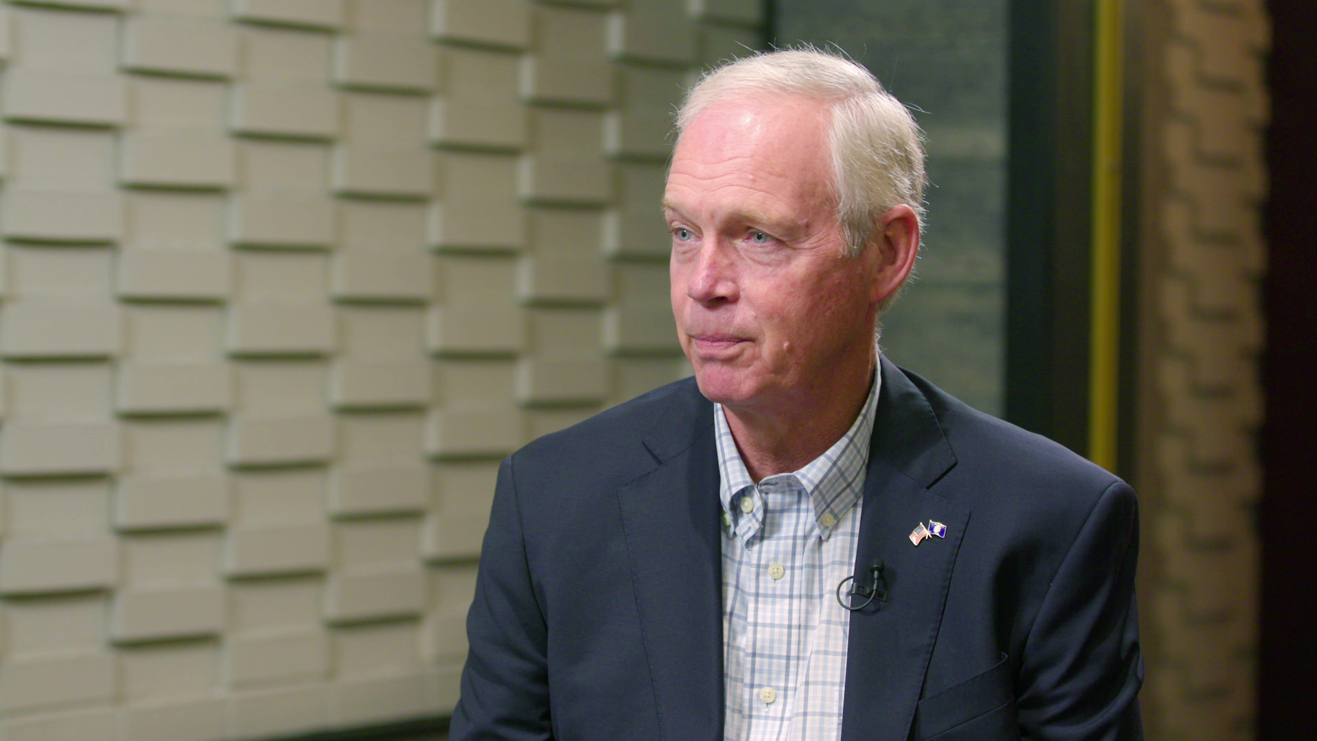 Ron Johnson speaks while looking to his side during an interview, with soundproofing materials on a wall in the background.