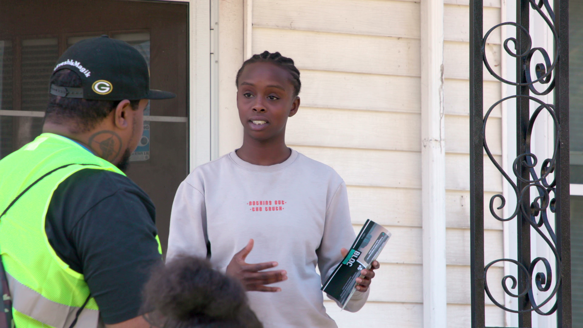 Miracle Holmes stands outside the front door of a house while gesturing with her hands and speaking two two people on its steps.