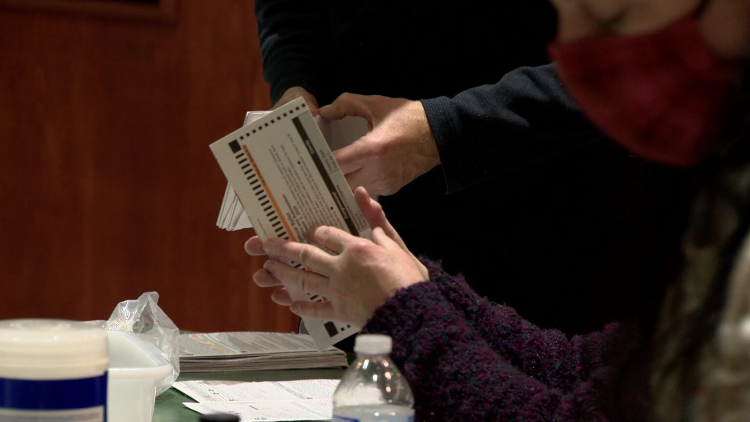 Elections workers open absentee ballots while seated and standing at a table.