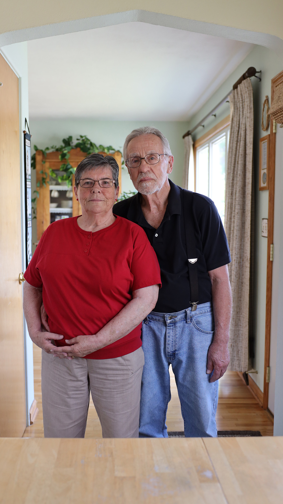 Jim Boisen and Margie Walker pose for a portrait inside a room, with a window, door and cabinet in the background.