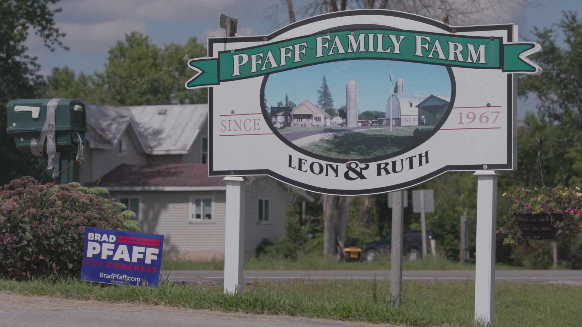 A sign that says "Pfaff Family Farm, since 1967, Leon and Ruth" with a Pfaff for Congress sign beside it. A mailbox and house are in the background.