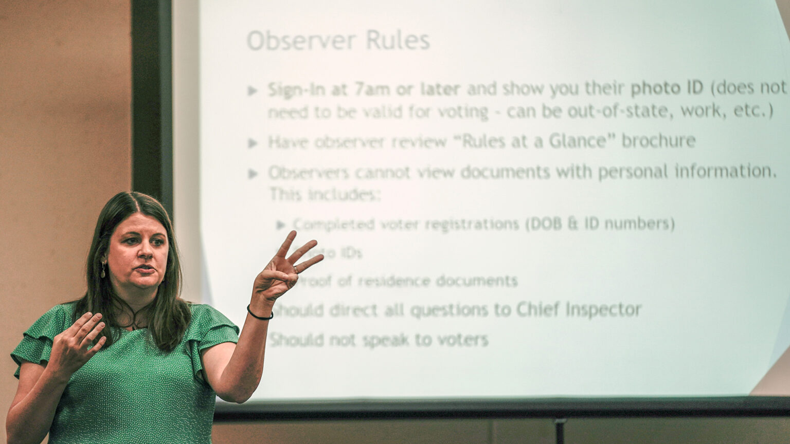 Claire Woodall-Vogg stands and gestures with her hands while standing in front of a projection screen showing a list of Observer Rules.