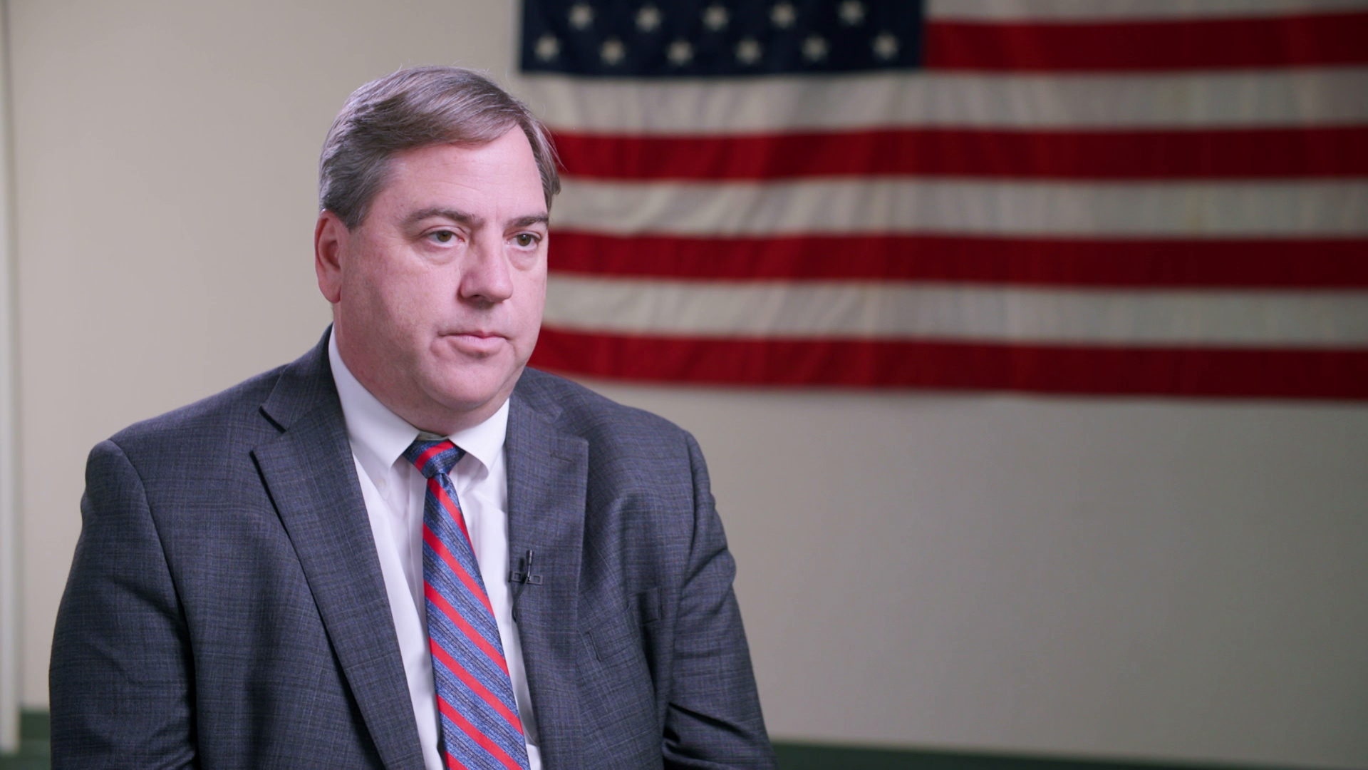 Paul Farrow sits in a room with a U.S. flag in the background.