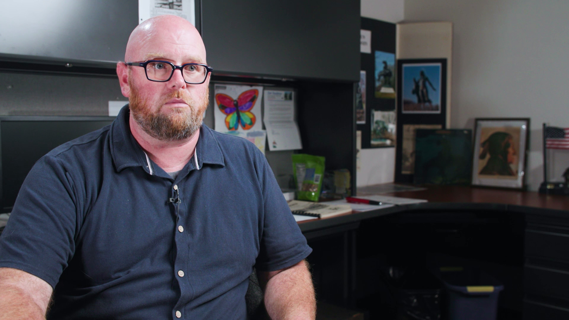 Rohn Bishop sits in an office with a desk and multiple pieces of art in the background.